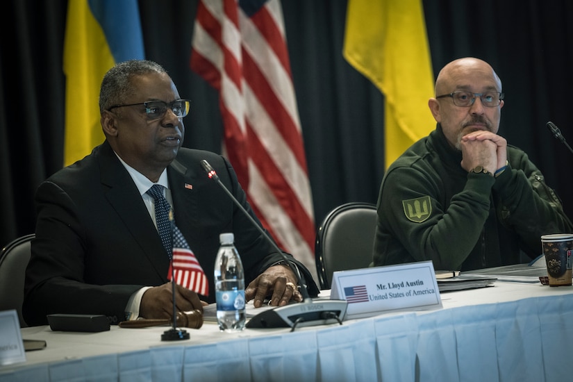 Secretary of Defense Lloyd J. Austin III and Ukrainian Defense Minister Oleksii Reznikov sit at a table with flags in the background.