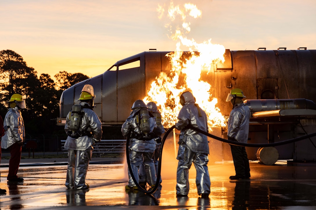 Sailors in firefighting gear try to put out flames.