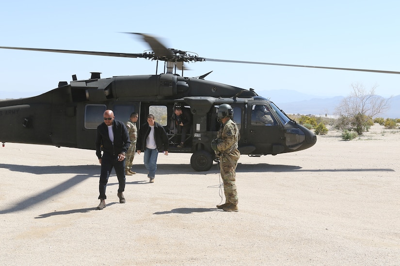 Two uniformed service members watch as several people exit a helicopter.