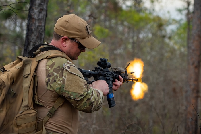 A cadre fires a semiautomatic weapon, revealing a bright burst and loose shell from its chamber.