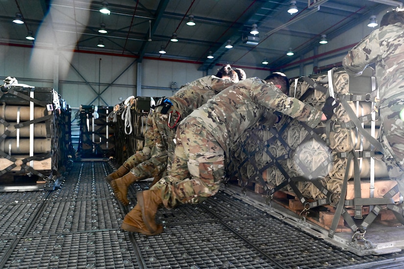 Men push cargo loaded on a pallet.