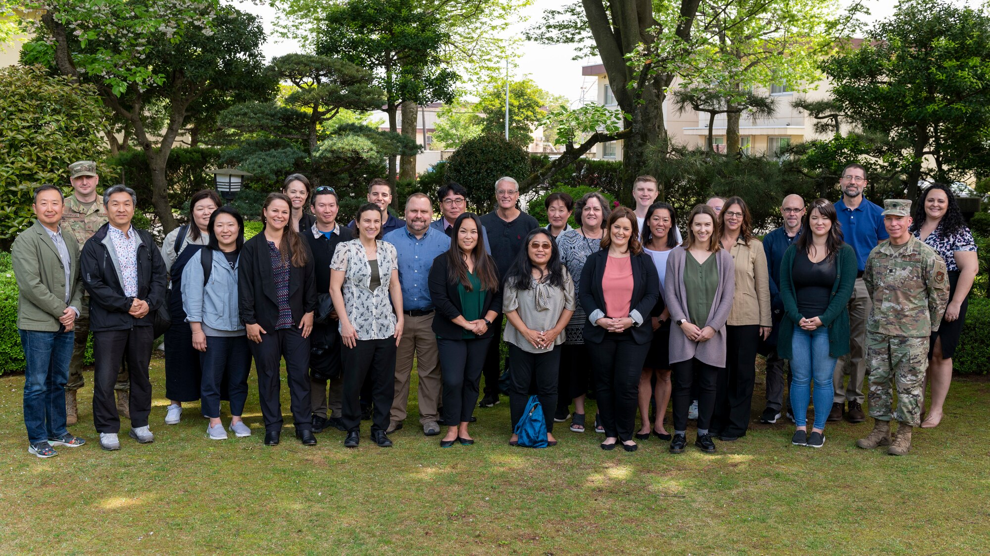 thirty people line up in a garden and pose for a group photo.