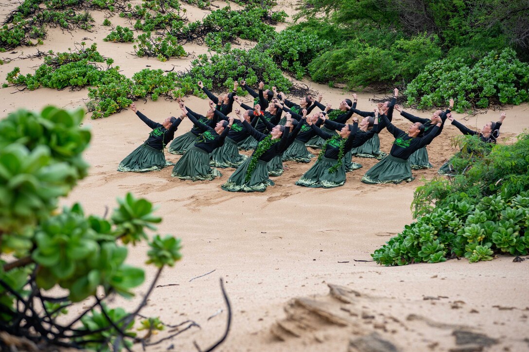 A group of hula performers dance in Hawaiian sand.