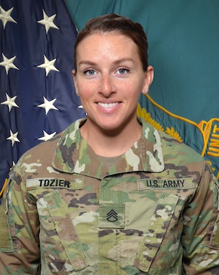 Woman in U.S. Army uniform standing in front of two flags.