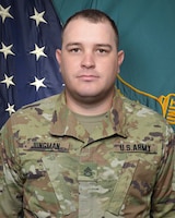 Man in U.S. Army uniform standing in front of two flags.