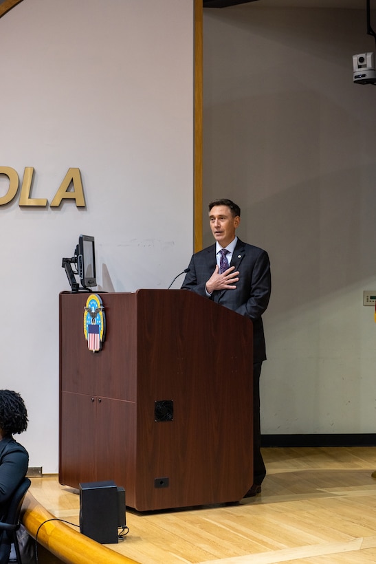 A light skinned man in a gray suit with graying hair speaks at a podium in an auditorium.