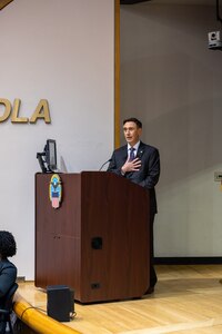 A light skinned man in a gray suit with graying hair speaks at a podium in an auditorium.
