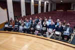 Men and women in business attire are seated with certificates in their hands in a auditorium.