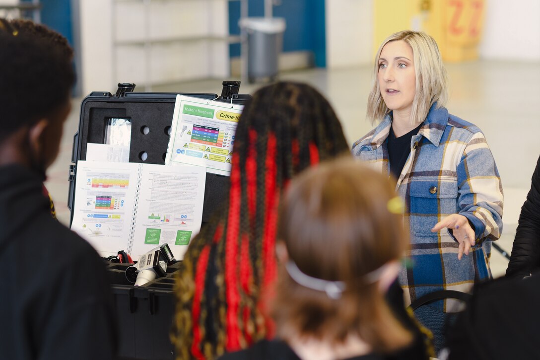 A woman speaks to a group of students in front of a exhibit.