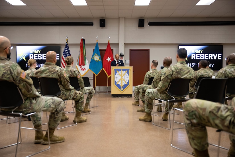 A group of Soldiers sitting, listen to a speaker standing at podium.
