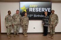 A group of five individuals stand and pose in front of a sign that says "Army Reserve 115th Birthday."