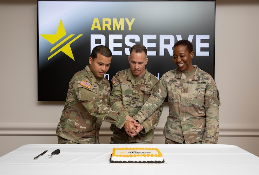 Three Soldiers cutting a cake together with a sword while standing.