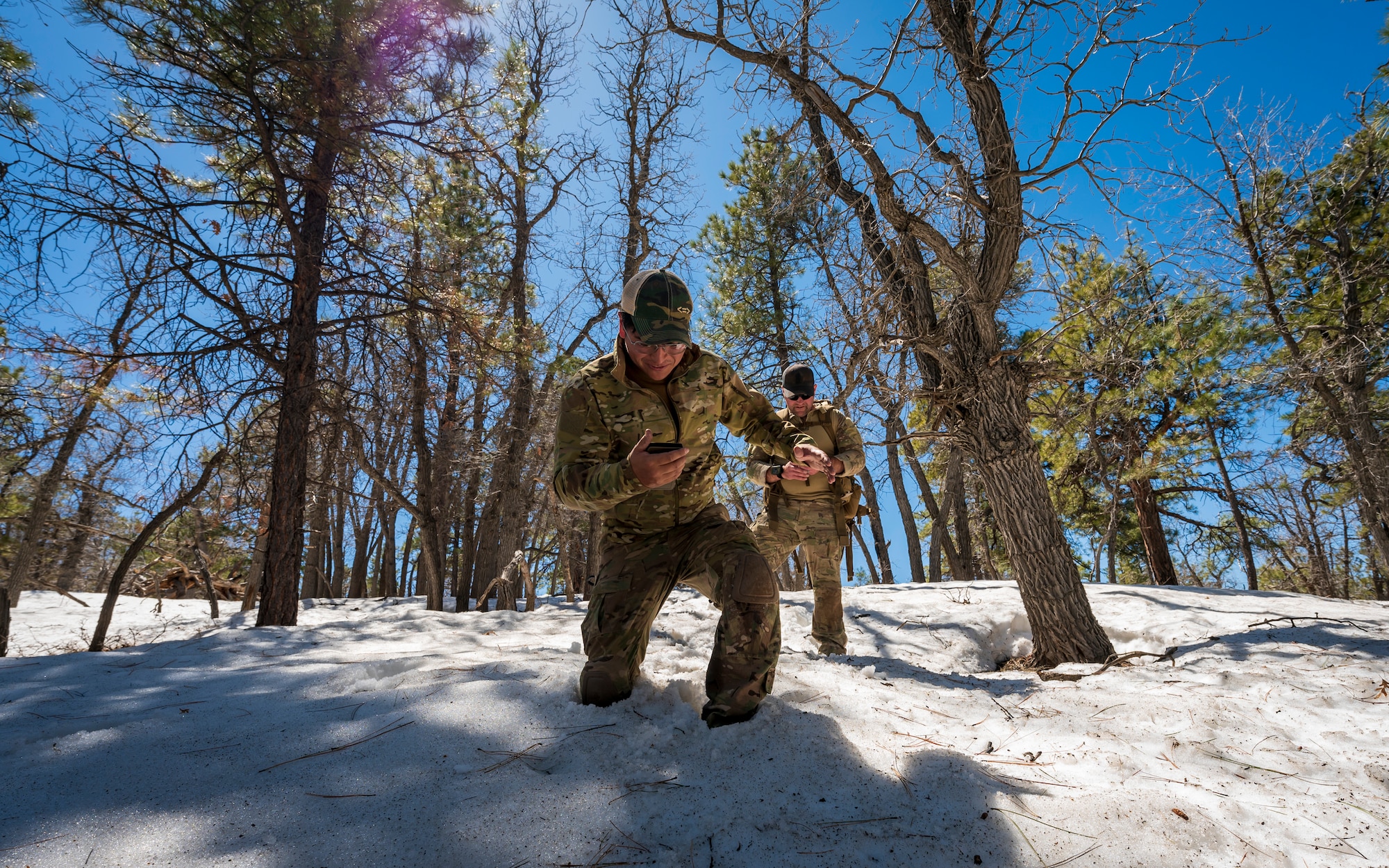 U.S. Air Force Tech. Sgt. Jason Evans (right) and Senior Airman Nestor Guevara-Penella (left), 56th Civil Engineer Squadron Explosive Ordnance Disposal flight technicians, hike down a snow-covered hill at Camp Navajo, Arizona, April 11, 2023.