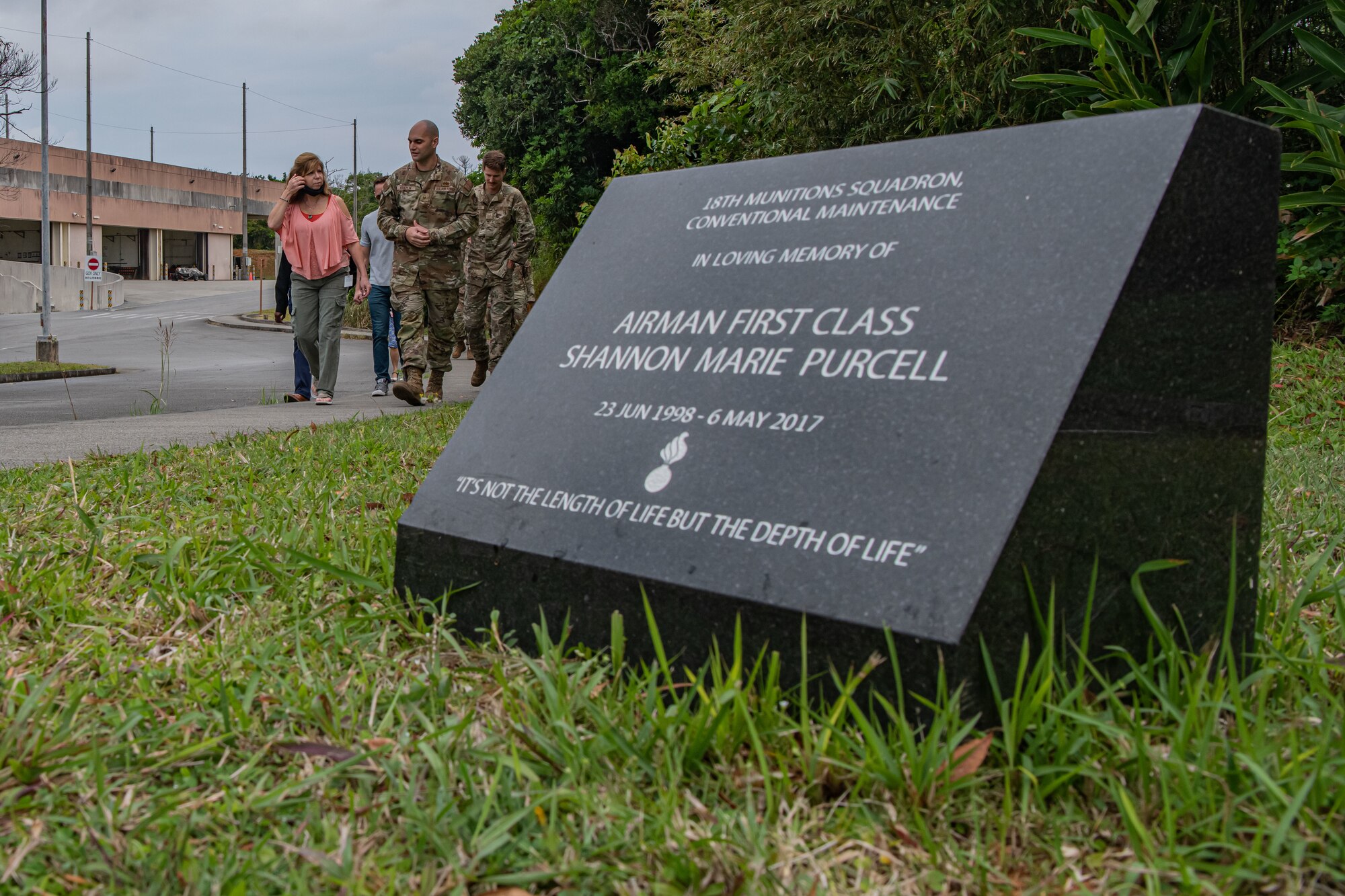 A memorial is in focus in the foreground while a group of people in the background walk toward it.