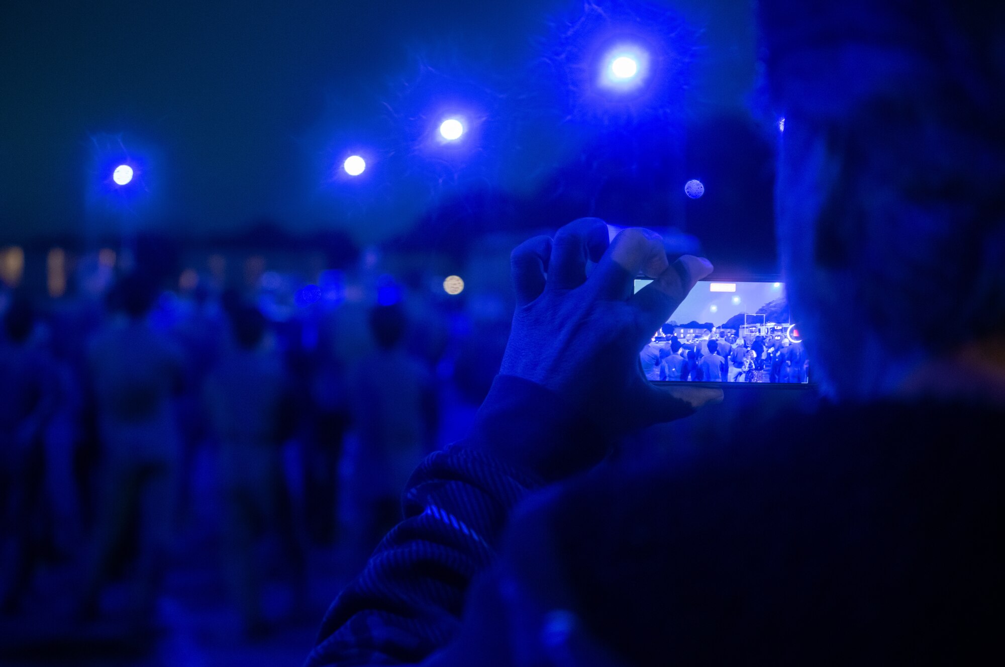 An individual holding a phone takes a photo of the piano burn. The light is blue due to the streetlights.