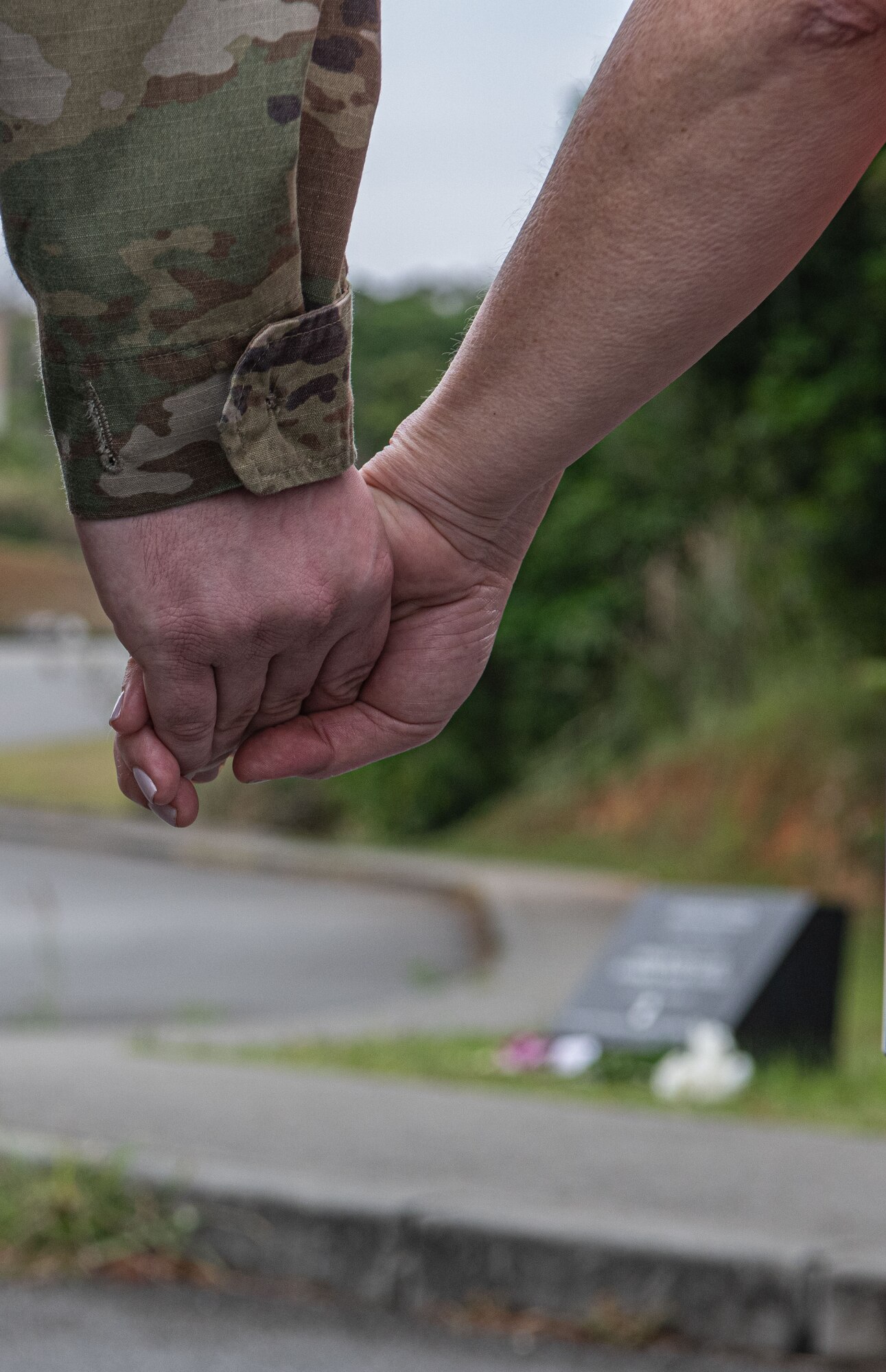 A man holds a woman's hand with a memorial in the background of the photo.