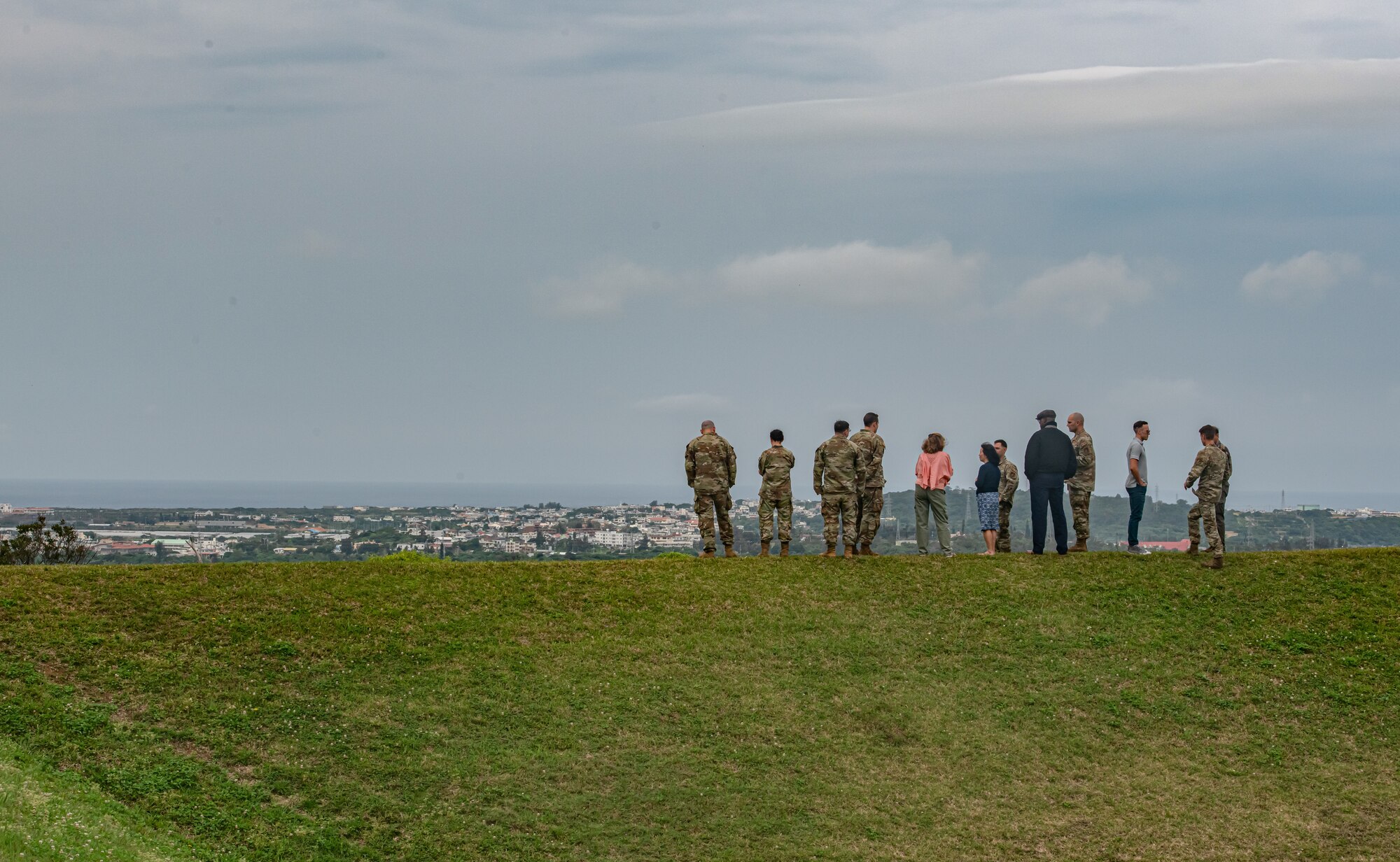 A wide shot of a group of people standing on a hill overlooking a city.