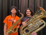 Two male students stand looking at the camera, one holds a sax the other holds a tuba.