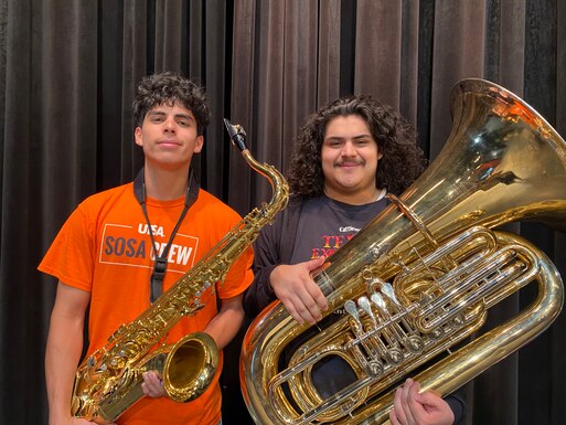 Two male students stand looking at the camera, one holds a sax the other holds a tuba.