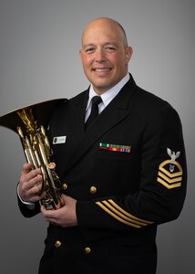 A man in a Navy uniform stands holding a French horn.