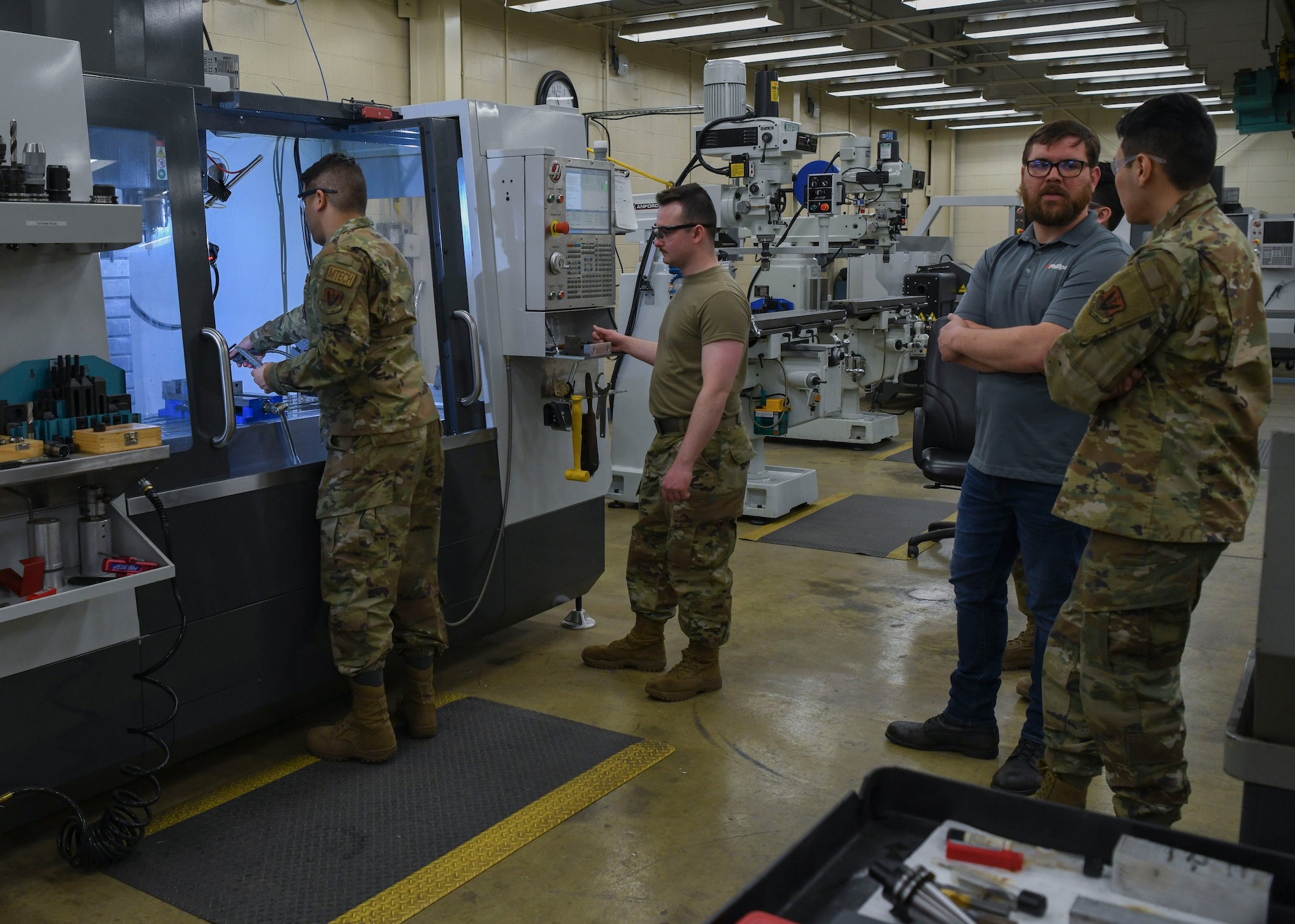 Several men stand around a room filled with metal working equipment.