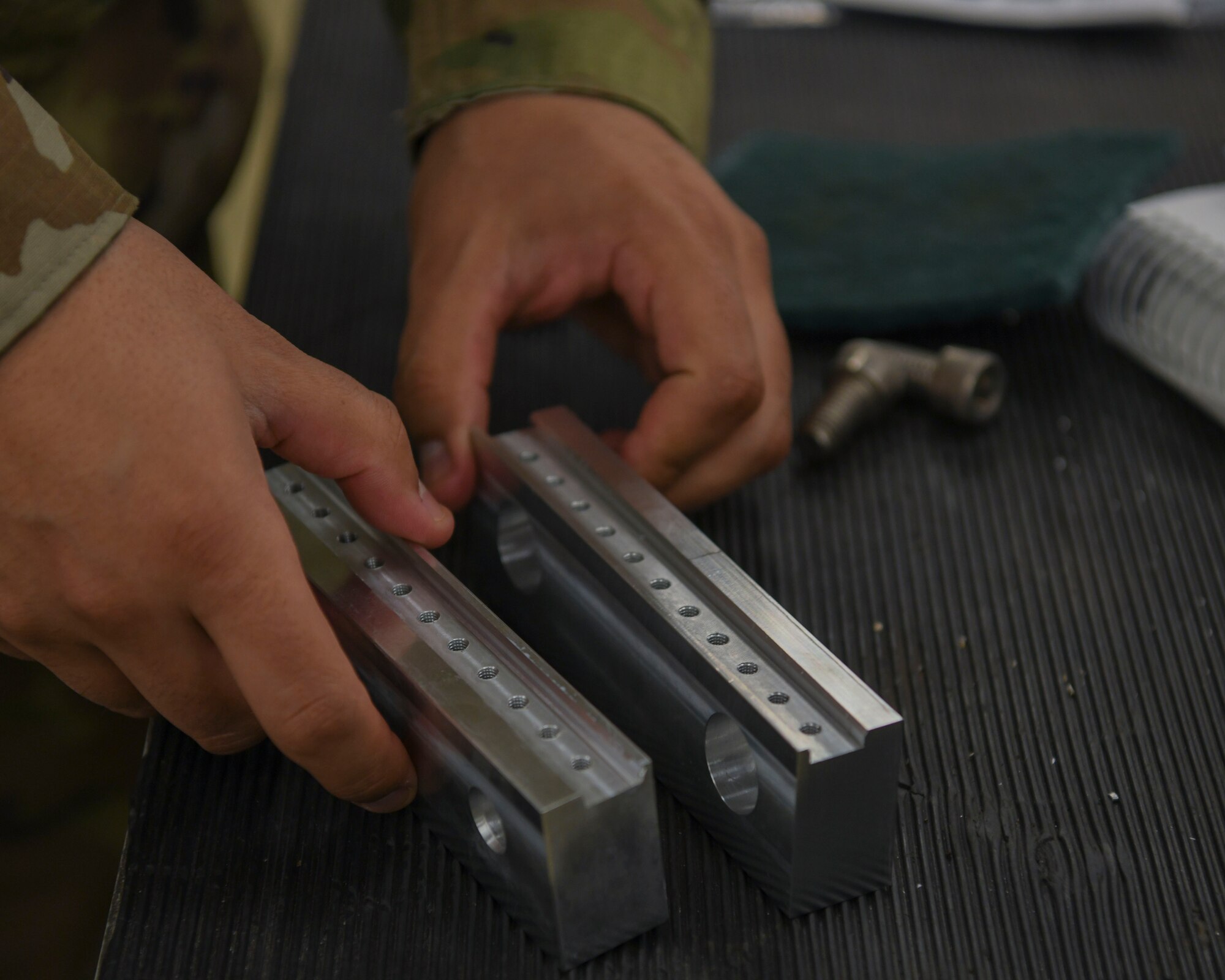 Two hands hold onto two pieces of metal that have holes drilled into them on a black table.