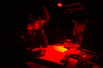 Quartermaster 3rd Class Anthony Phillips writes in the ship's log on the bridge of the guided-missile destroyer USS Paul Hamilton (DDG 60), April 23 in the Gulf of Oman.