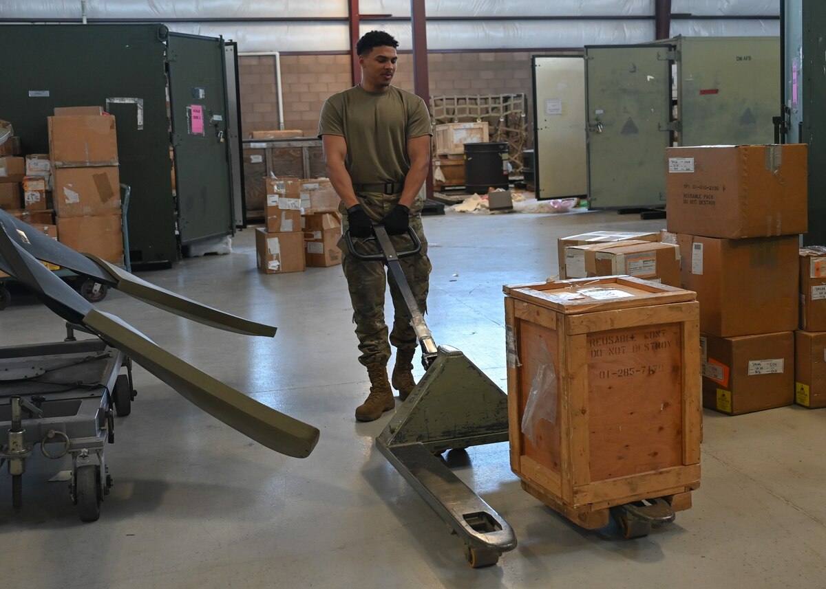 A man in a military uniform moves a wooden crate.