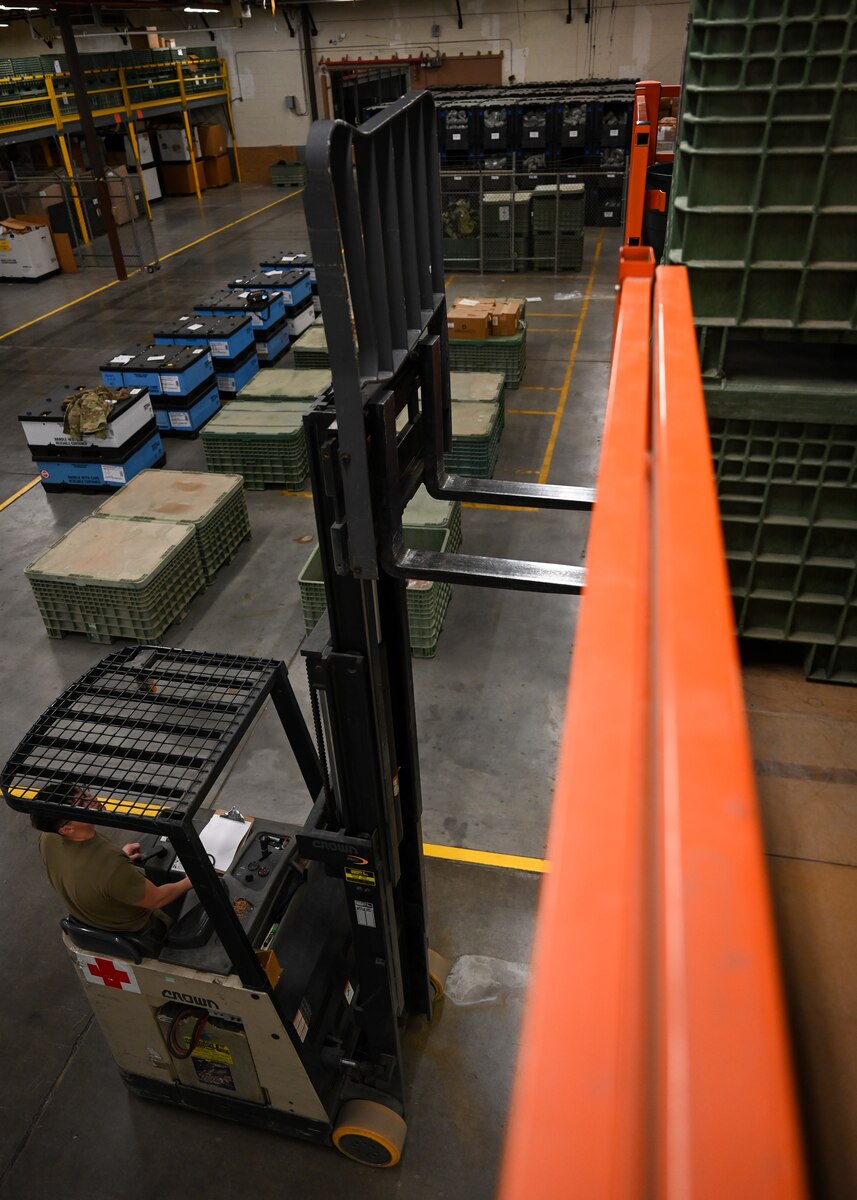 A man in a military uniform operates a forklift to move crates.