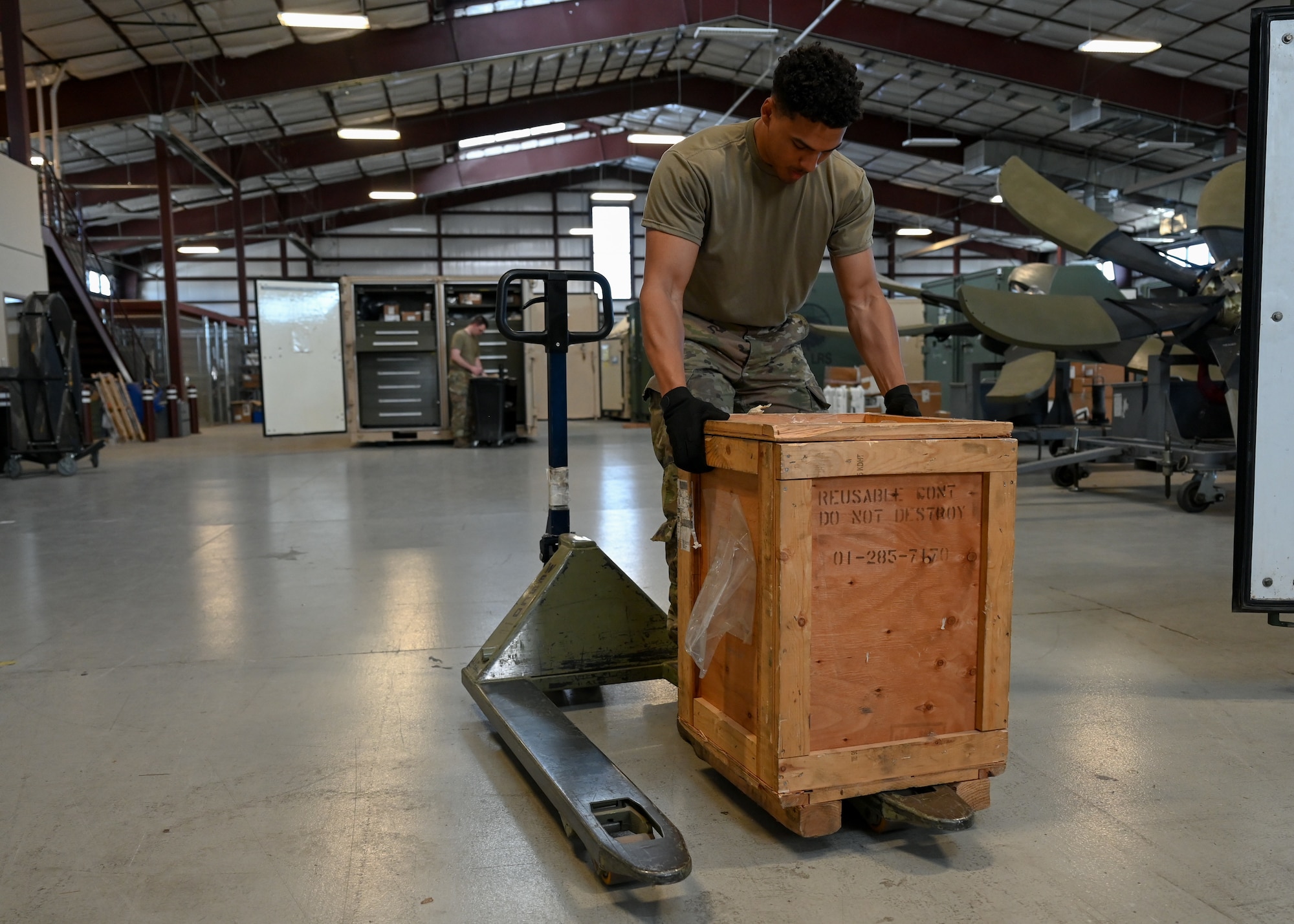 A man in a military uniform moves a wooden crate.