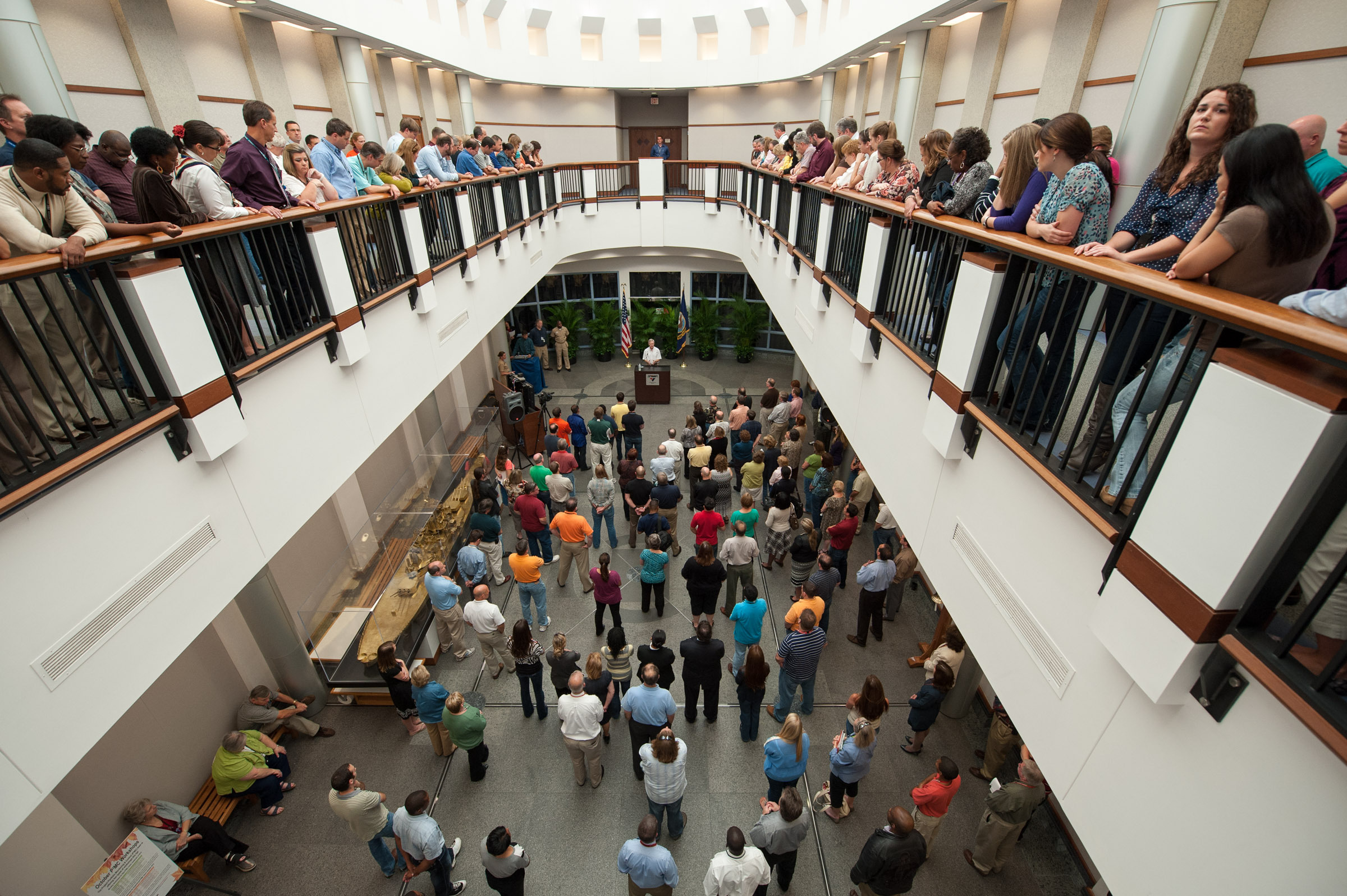 A crowd of people overlooking the atrium from the second floor watching the Secretary of the Navy