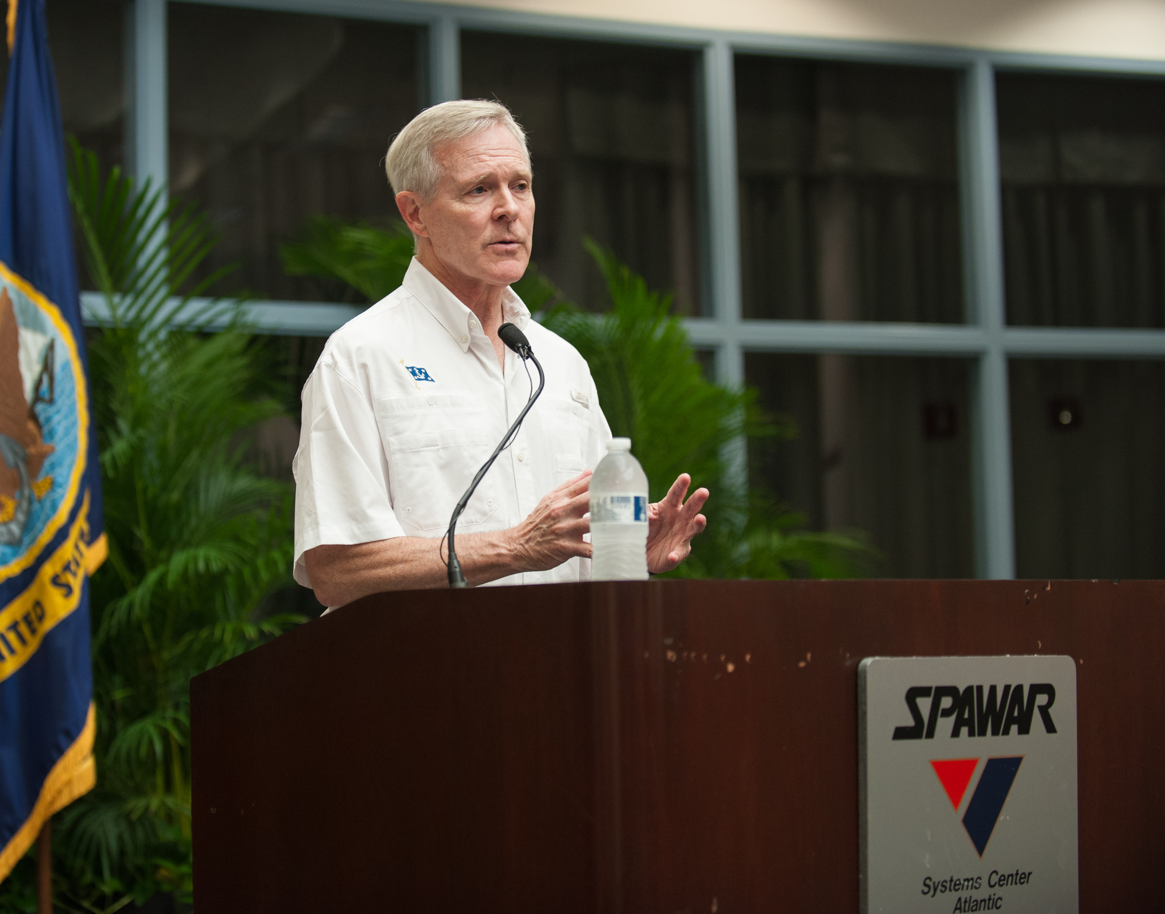 Secretary of the Navy speaking at a podium in an atrium
