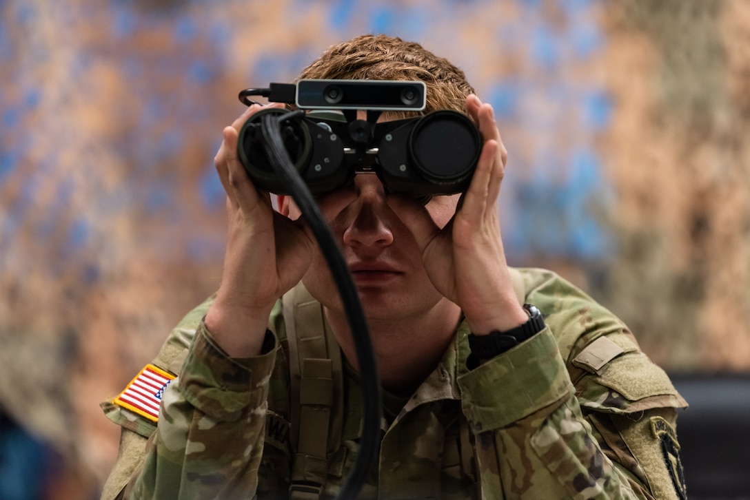 A soldier is shown looking through binoculars.