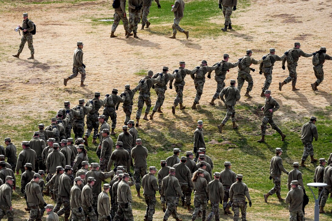 Air Force cadets run in a line while holding onto the person in front of them in a field.