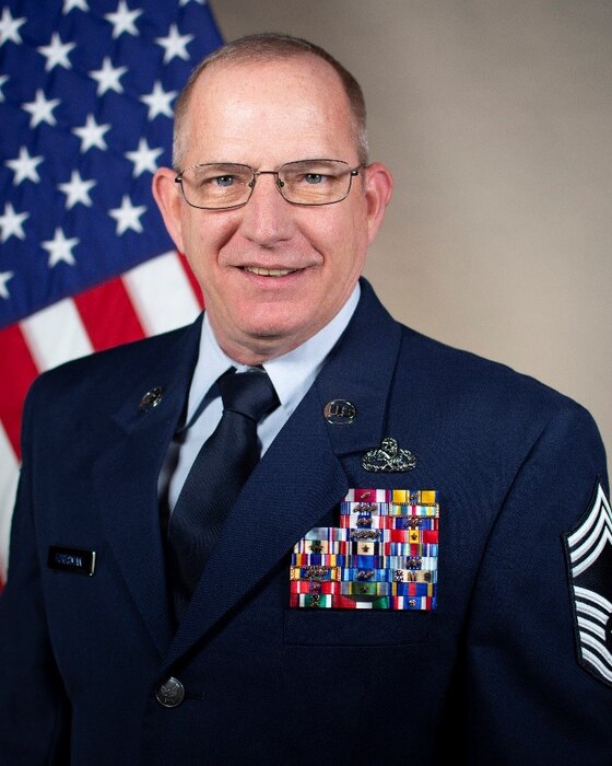 Service member smiles for official portrait in front of US flag wearing his service dress