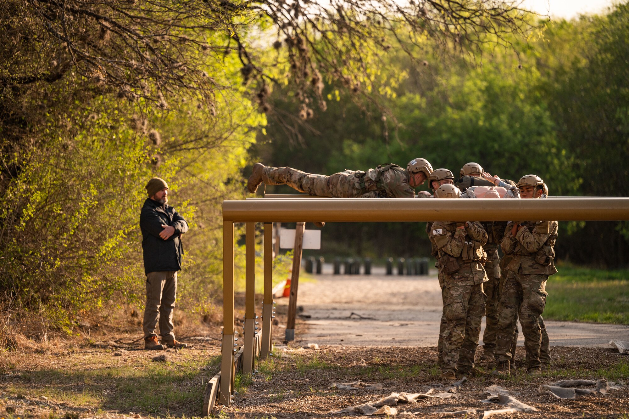 instructor watches as Airman jumps over raised log