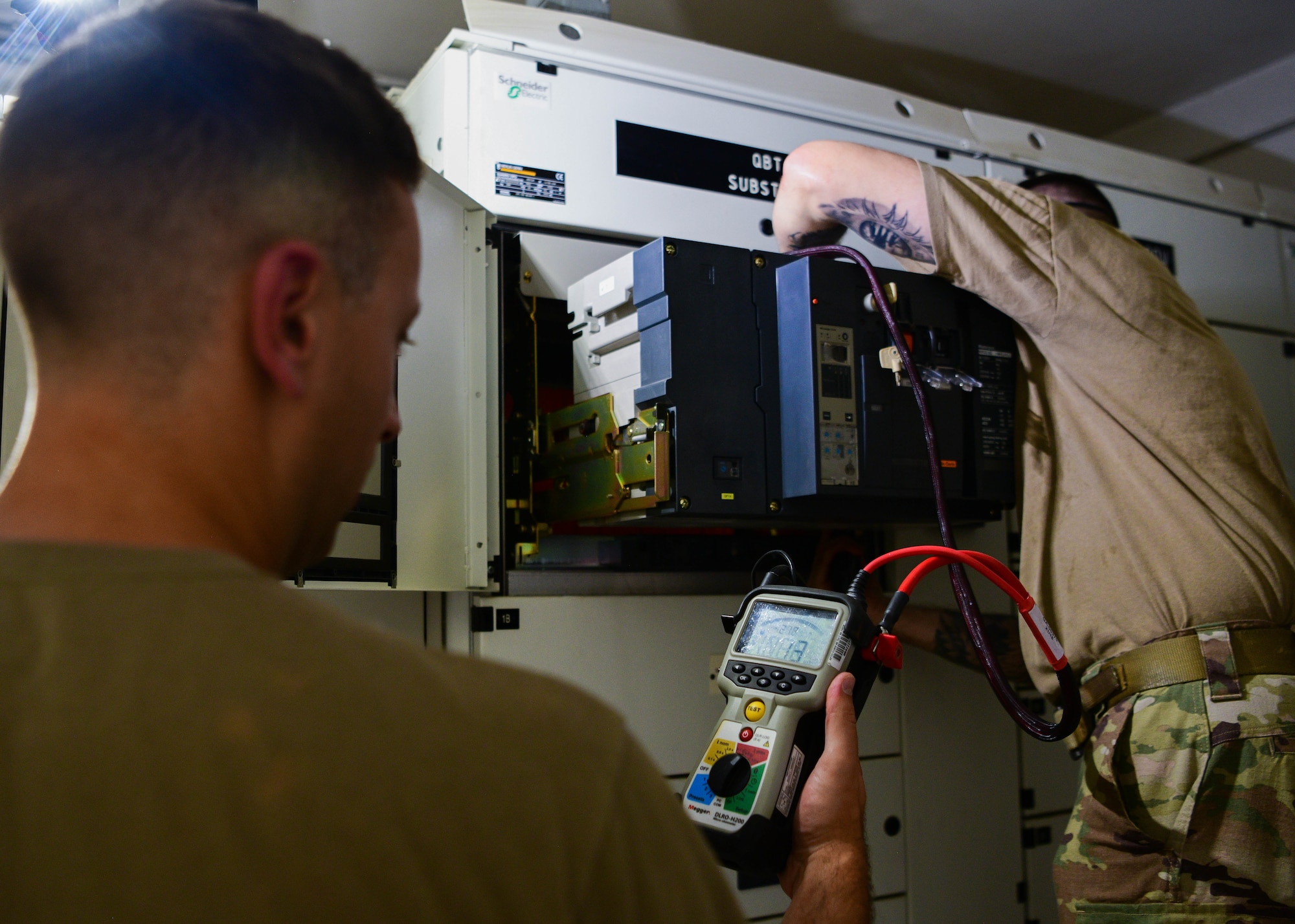 One man works on an electrical box while  another monitors voltage.