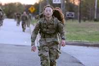 A female Soldier walks in the middle of the street with her ruck sack in the early morning light.