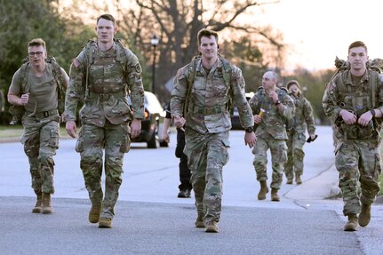 Soldiers walking down the middle of the street with ruck sacks in the early morning light.