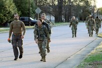 Soldiers and civilians walking in the middle of a street with ruck sacks in the morning.