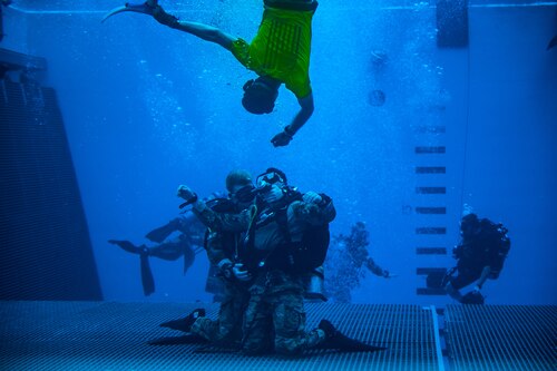Instructor swims to bottom of pool where two dive students buddy breathe