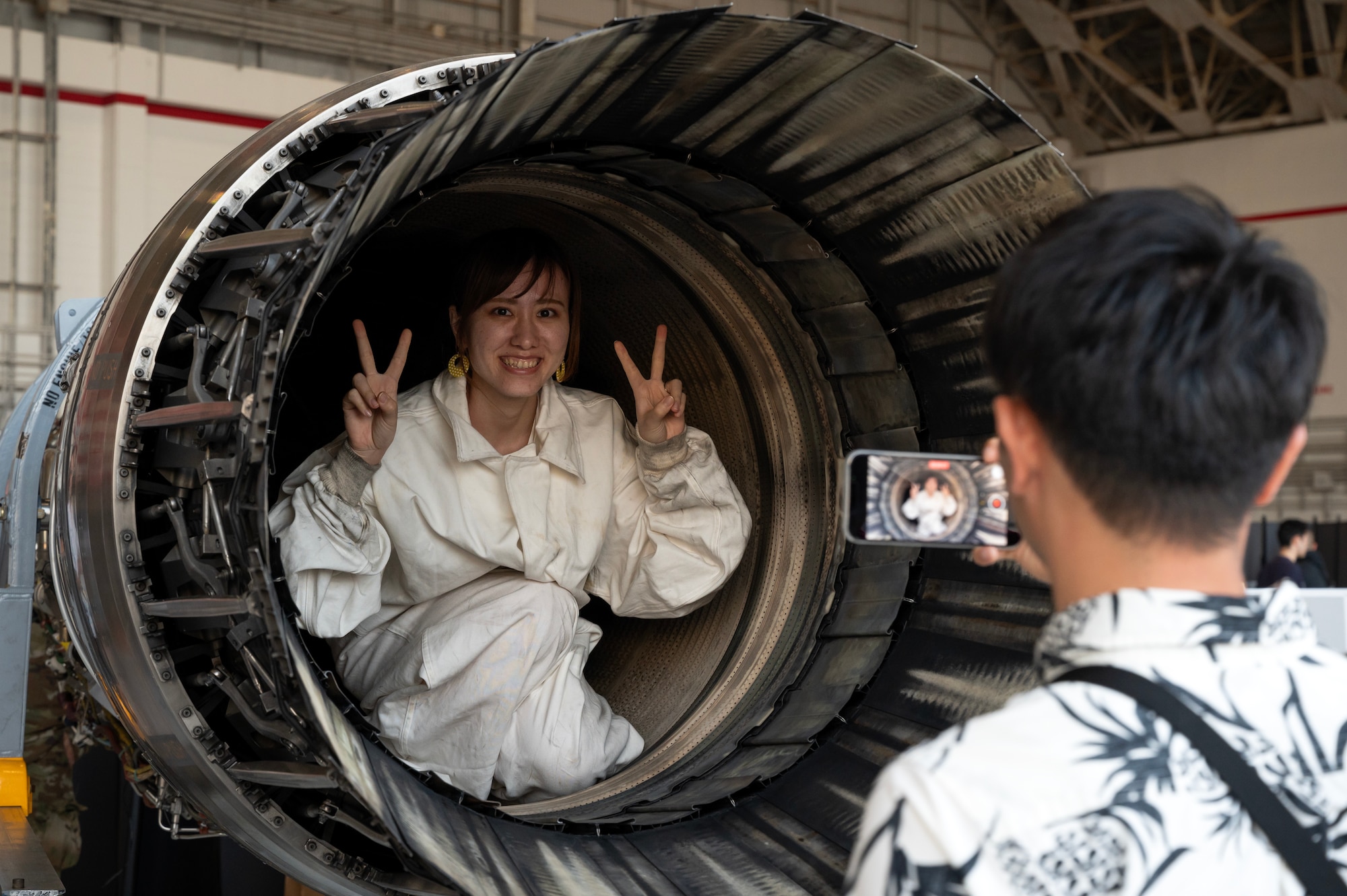An America Fest 2023 attendee poses for a photo in an F-15C Eagle engine static display at Kadena Air Base, Japan, April 23, 2023. America Fest gave local community members the opportunity to meet U.S. service members, learn about their role in the defense of Japan and experience American culture. (U.S. Air Force photo by Senior Airman Jessi Roth)