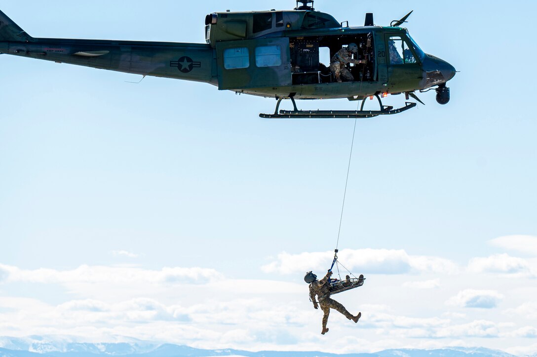 An airman and a litter are cabled up to a helicopter.