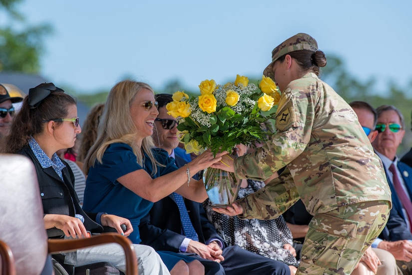 A soldier gives a bouquet of yellow roses to a woman.