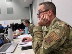 man looks at laptop computer, head resting on hand.