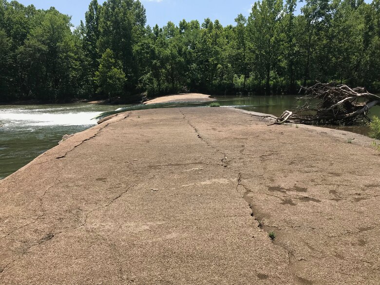 A rock outcrop sits in a river as water flows through the middle of it.