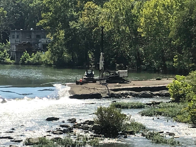 A piece of heavy machinery sits on a rock outcrop in a river.