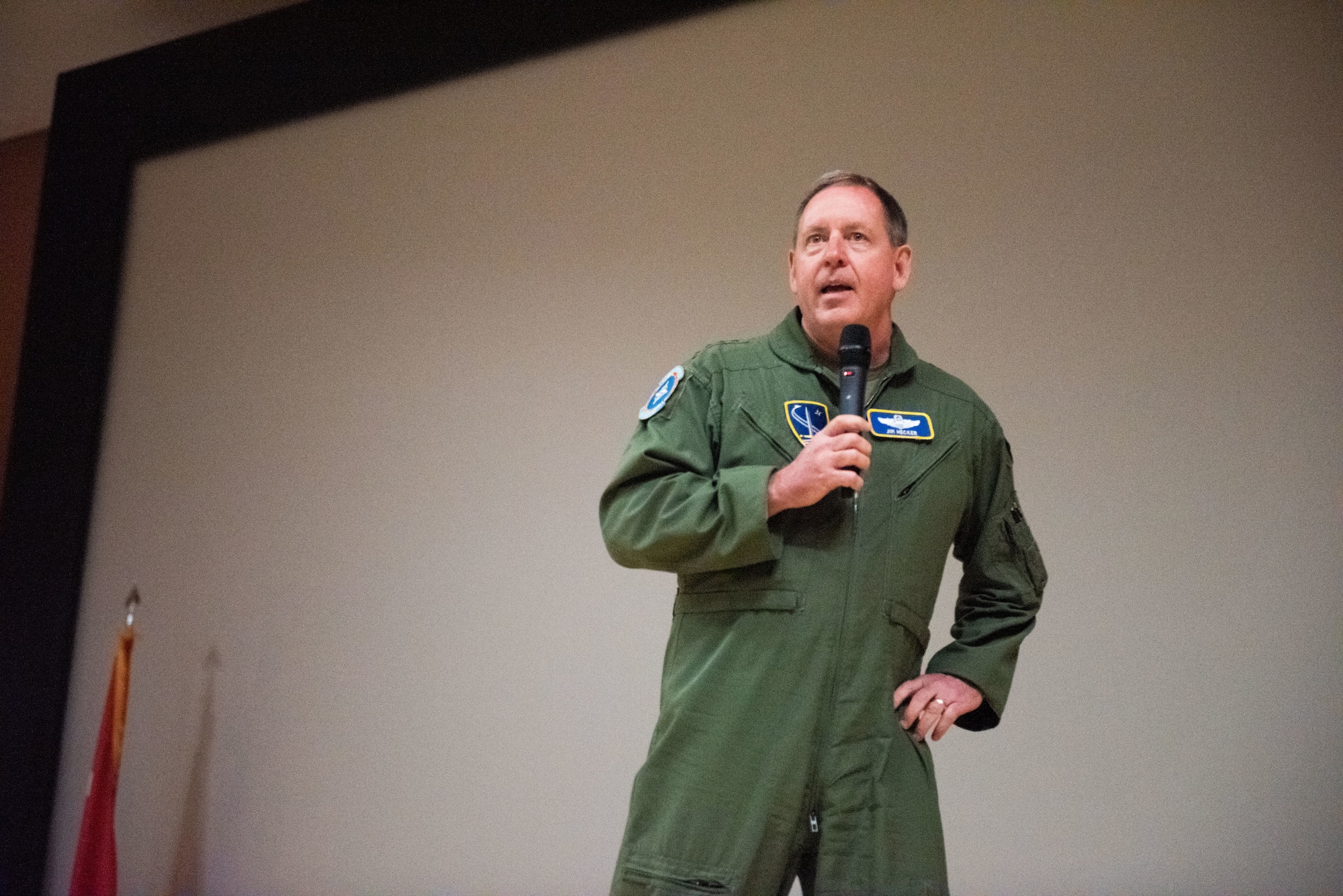 A man in a green flight suit speaks into a microphone.