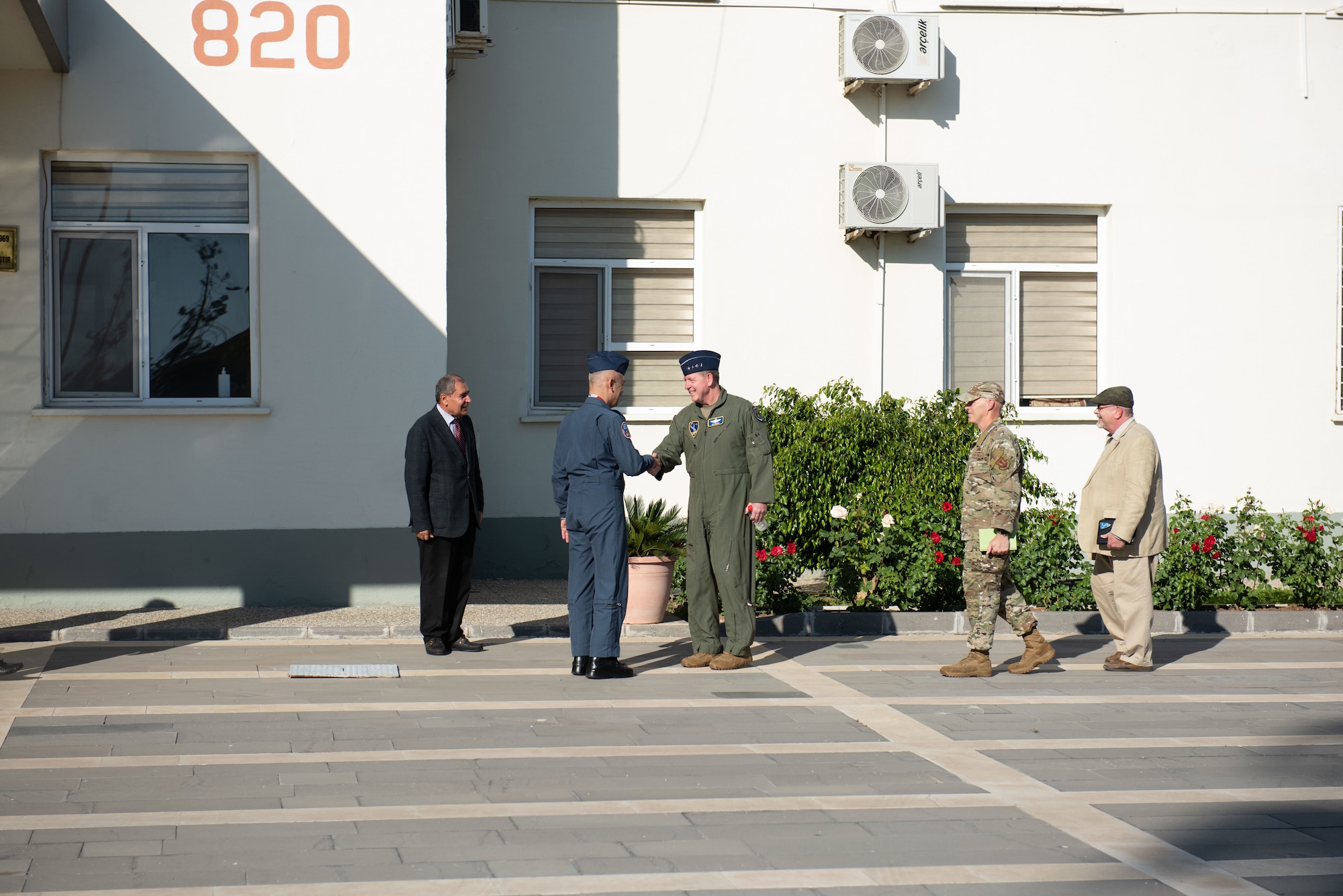 Two men shake hands outside of a building.