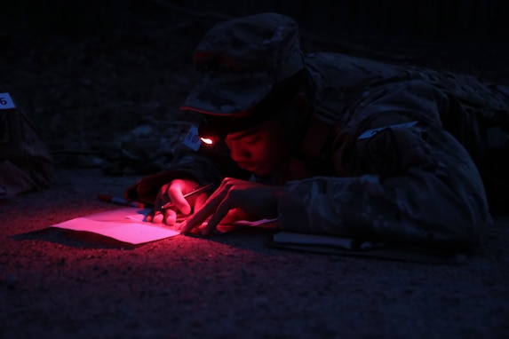 Cadet Justin Dungca of the 414th Chemical Company, 457th Chemical Battalion plots points on a map after dusk to prepare for the night land navigation course event at the 76th ORC's Best Warrior Competition on March 27, 2023 at Fort Lee, Virginia.